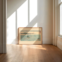 Japanese whirlpools and coastal seascape print in an oak frame on a sunlit wood floor beneath tall window light