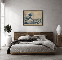 Great wave with boats and Mount Fuji print in a dark wood frame above a rattan bed on a plaster wall