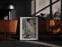 Black-framed Japanese waterfall with travelers and hut print on a moody console with designer coffee-table books