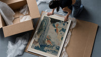 Japanese waterfall with travelers and hut framed print being unpacked from protective bubble wrap and a box