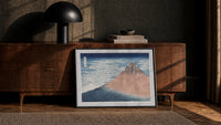 Mount Fuji with snow-capped peak print in a black frame leaning against a walnut console in lamplight
