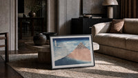 Mount Fuji with snow-capped peak print in a slim black frame leaning on a travertine coffee table