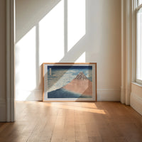 Mount Fuji with snow-capped peak print in an oak frame on a sunlit wood floor beneath tall window light