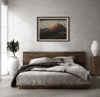 Mount Fuji with lightning storm print in a dark wood frame above a rattan bed on a plaster wall