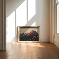 Mount Fuji with lightning storm print in an oak frame on a sunlit wood floor beneath tall window light