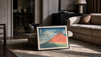 Red Mount Fuji with clouds print in a slim black frame leaning on a travertine coffee table