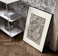 Death leading a robed figure poster in a black frame leaning beside a shelf in a raw-plaster loft
