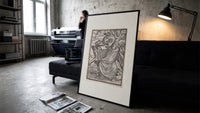 Death leading a robed figure print in a slim black frame leaning on a dark sofa in a concrete print studio