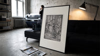 Death and two noblewomen print in a slim black frame leaning on a dark sofa in a concrete print studio