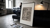 Death fighting armored nobleman print in a slim black frame leaning on a dark sofa in a concrete print studio
