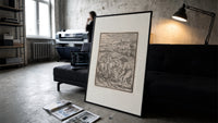 Death plowing field with farmer print in a slim black frame leaning on a dark sofa in a concrete print studio