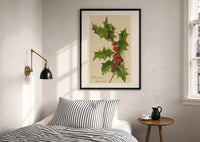 Holly Christmas Greetings print in a black frame above a bed with striped linens, a brass wall lamp and a sunlit window