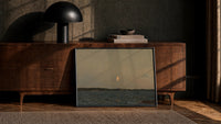 moonrise over calm sea vintage art print print in a black frame leaning against a walnut console in lamplight