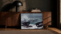 wave crashing on rocky coast vintage art print print in a black frame leaning against a walnut console in lamplight
