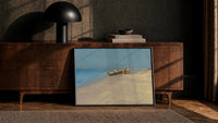 fishermen hauling a boat ashore vintage art print print in a black frame leaning against a walnut console in lamplight
