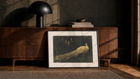 peacock in a moonlit garden vintage art print print in a black frame leaning against a walnut console in lamplight