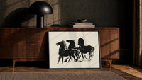 three horses in bold silhouette vintage art print print in a black frame leaning against a walnut console in lamplight