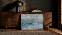 ocean waves and clouds vintage art print print in a black frame leaning against a walnut console in lamplight