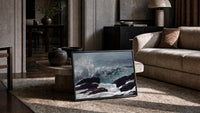 wave crashing on rocky coast vintage art print print in a slim black frame leaning on a travertine coffee table