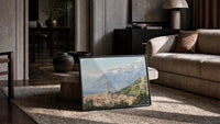 Italian hillside village below snow-capped Alps vintage art print print in a slim black frame leaning on a travertine…
