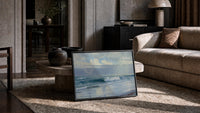 ocean waves and clouds vintage art print print in a slim black frame leaning on a travertine coffee table