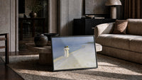 two women in white walking a beach at dusk vintage art print print in a slim black frame leaning on a travertine coffee table