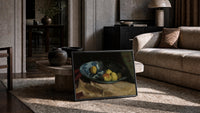 apples and quince in a porcelain bowl vintage art print print in a slim black frame leaning on a travertine coffee table