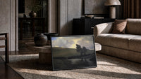 rolling hills, pond, and windswept trees under dramatic clou vintage art print print in a slim black frame leaning on a…