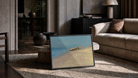 fishermen hauling a boat ashore vintage art print print in a slim black frame leaning on a travertine coffee table