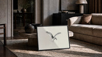 seagull in flight, pencil sketch vintage art print print in a slim black frame leaning on a travertine coffee table