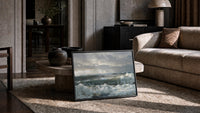 storm waves crashing on a rocky shore vintage art print print in a slim black frame leaning on a travertine coffee table
