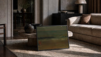 figures on a beach before crashing surf vintage art print print in a slim black frame leaning on a travertine coffee table