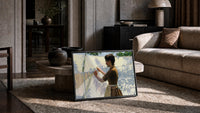 woman hanging laundry in sunlight vintage art print print in a slim black frame leaning on a travertine coffee table