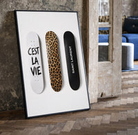 Saint Laurent Cest La Vie Skateboards framed poster print in a black frame leaning beside a vintage door on parquet
