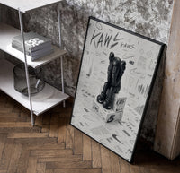 KAWS Companion Nike Swoosh Sketch framed poster poster in a black frame leaning beside a shelf in a raw-plaster loft