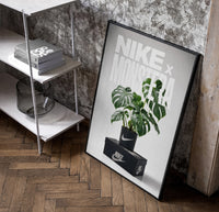Nike Monstera Sneaker framed poster poster in a black frame leaning beside a shelf in a raw-plaster loft