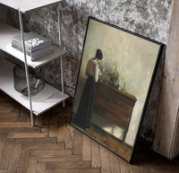 woman reading at a dresser in a quiet interior vintage art print poster in a black frame leaning beside a shelf in a…