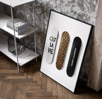 Saint Laurent Cest La Vie Skateboards framed poster poster in a black frame leaning beside a shelf in a raw-plaster loft