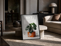 Nike Monstera Sneaker Box Green framed poster print in a black frame leaning on a travertine table in a sunlit lounge