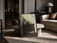 woman reading at a dresser in a quiet interior vintage art print print in a black frame leaning on a travertine table in…