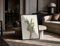 juniper branch with berries vintage art print print in a black frame leaning on a travertine table in a sunlit lounge