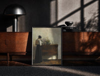 Black-framed woman reading at a dresser in a quiet interior vintage art print print on a moody console with designer…