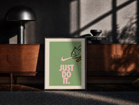 Black-framed Just Do It Chameleon Green Pink print on the floor in front of a dark wooden console