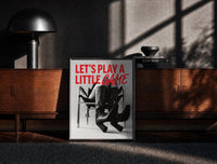 Black-framed Let's Play a Little Game print on the floor in front of a dark wooden console