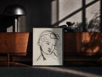 Black-framed woman's head in flowing contour lines vintage art print print on a moody console with designer coffee-table…