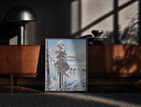 Black-framed ice skaters on a frozen lake among snowy pines vintage art print print on a moody console with designer…