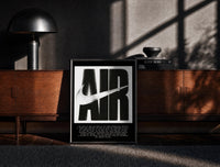 Black-framed Nike Air History framed poster print on a moody console with designer coffee-table books