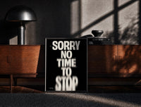 Black-framed Sorry No Time To Stop print on the floor in front of a dark wooden console
