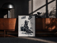 Black-framed Nike x KAWS Air Force 1 print on the floor in front of a dark wooden console