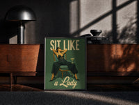 Black-framed Sit Like a Lady print on the floor in front of a dark wooden console